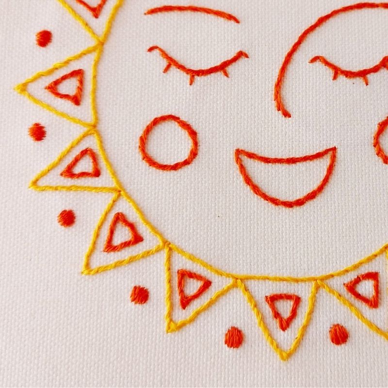 Diseño de sol feliz bordado a mano sobre lienzo de algodón blanco roto