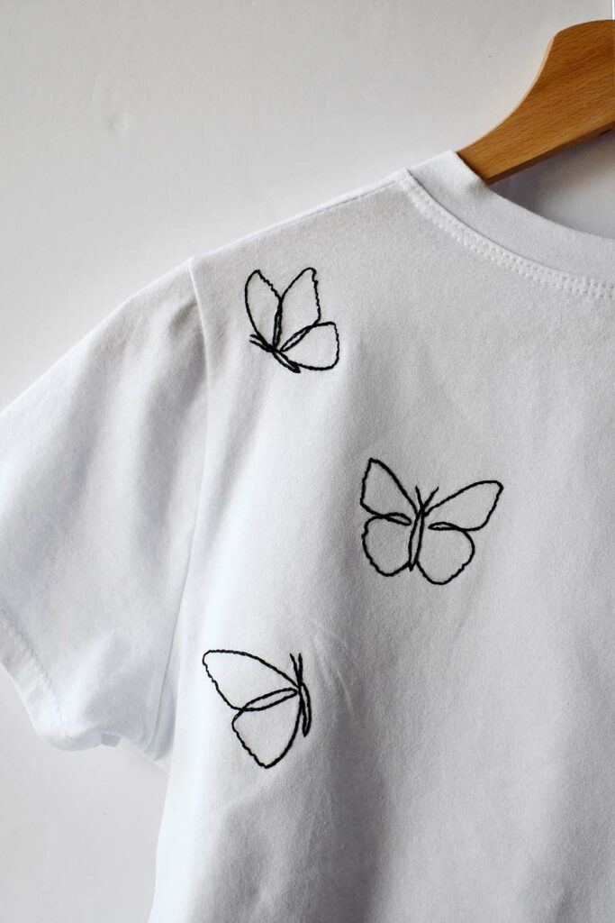 Camisetas blancas con mariposas bordadas a mano. Hilo de bordar negro, sólo contornos.
