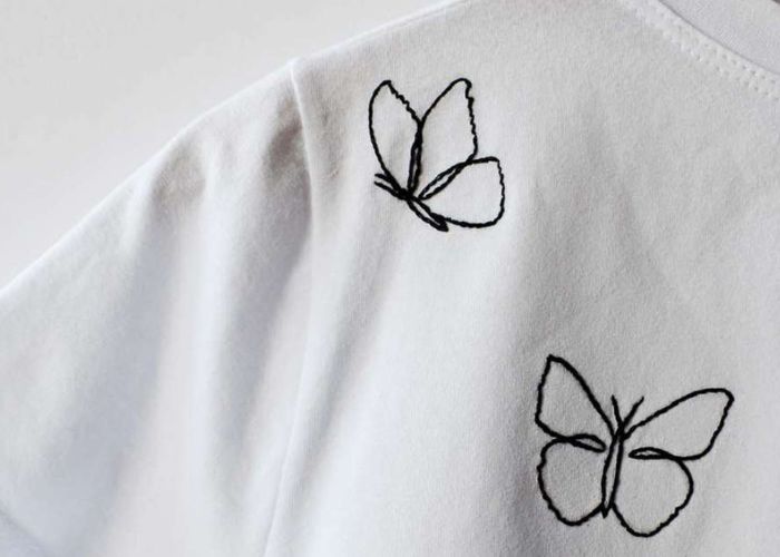 Contorno de mariposa negro bordado en camiseta blanca