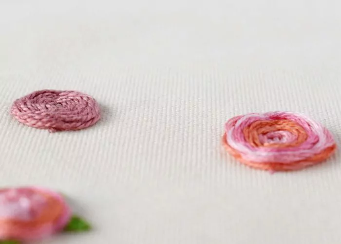 Flores rosas bordadas a mano con punto de rueda tejida sobre tela blanca