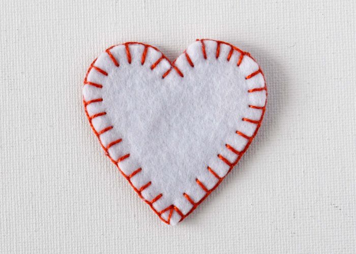 Puntada de manta para coser adorno de corazón de fieltro blanco